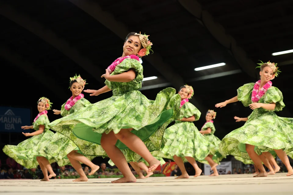 Hula dancers smiling as they perform in green dresses.