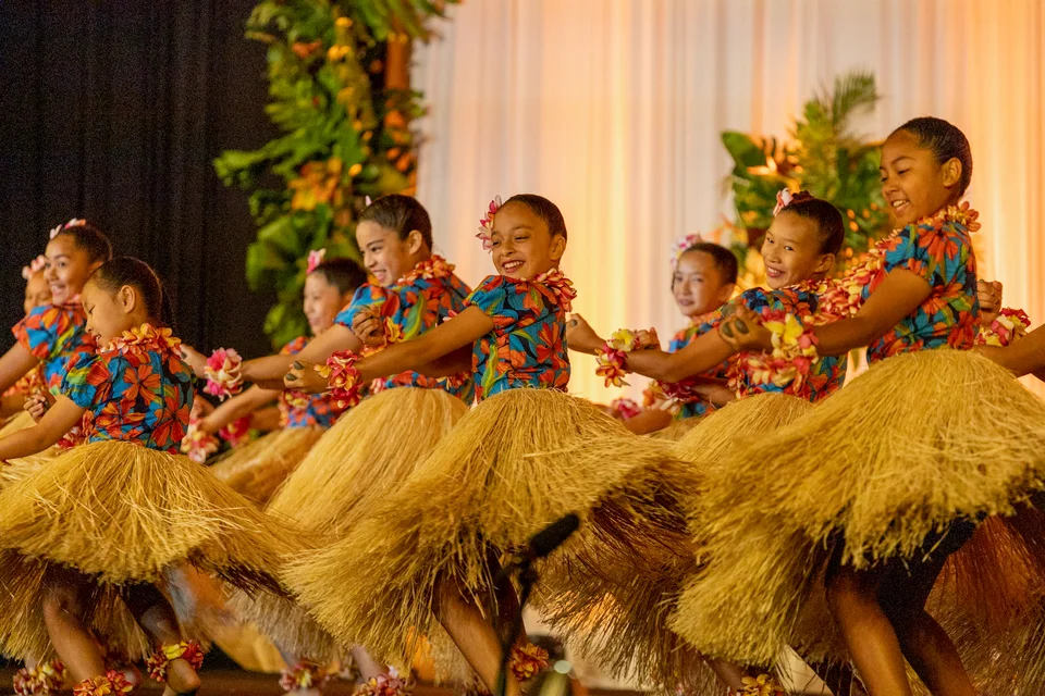 Young hula dancers seated together during a performance.